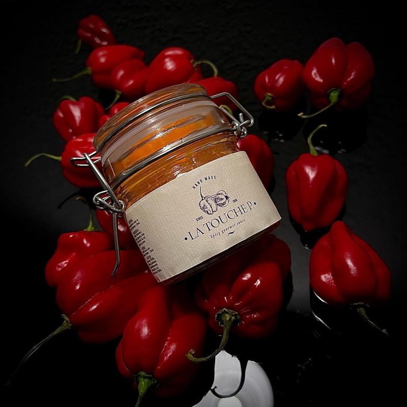 Ein Glas La Touche P. umgeben von roten Habanero-Chilis