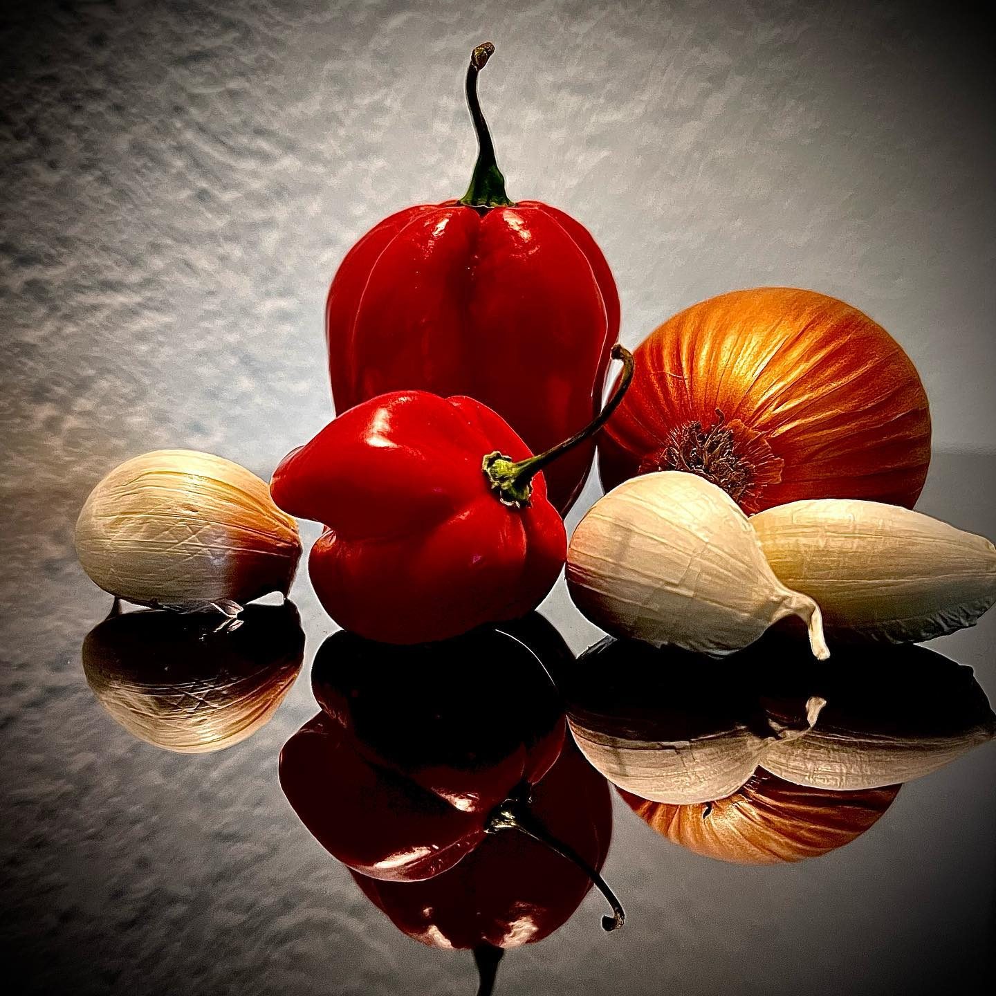 Habanero-Chilis, Zwiebel und Knoblauch auf spiegelnder Fläche